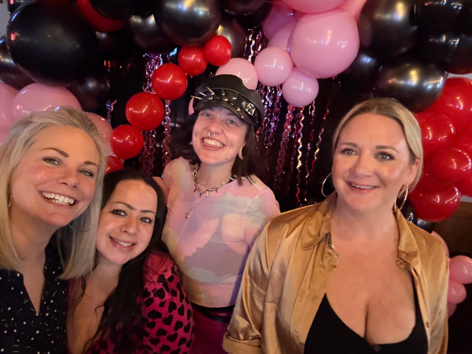 Four friends celebrating at Dax's surrounded by pink, red and black balloons