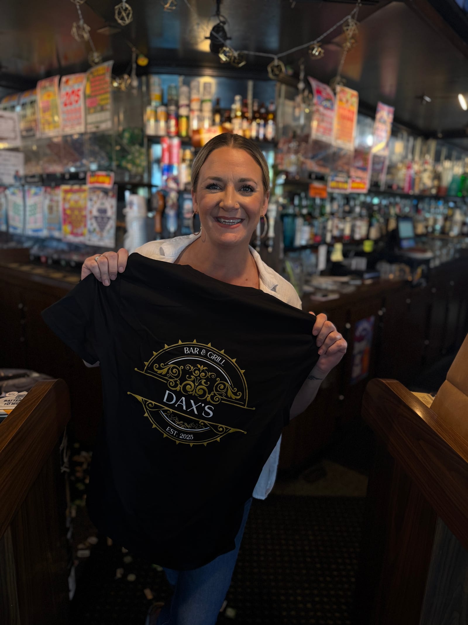 A member of the Dax's team behind the bar holding up a Dax's Bar & Grill t-shirt